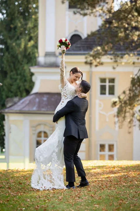 Bräutigam hebt die Braut lachend in die Luft, Gartenhochzeit vor dem Schloss