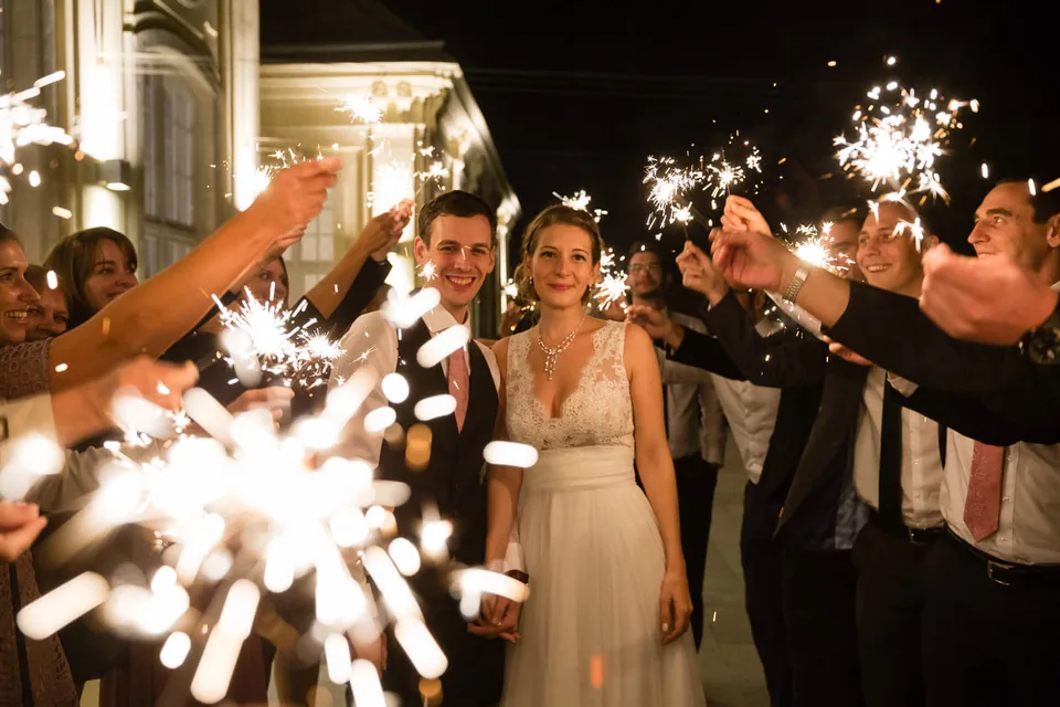 Hochzeitspaar zwischen Gästen mit Wunderkerzen am Abend