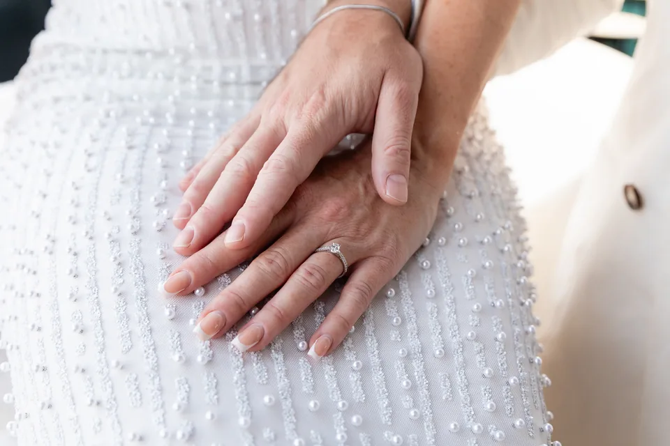 Hands of the newly engaged couple with the engagement ring on a white dress